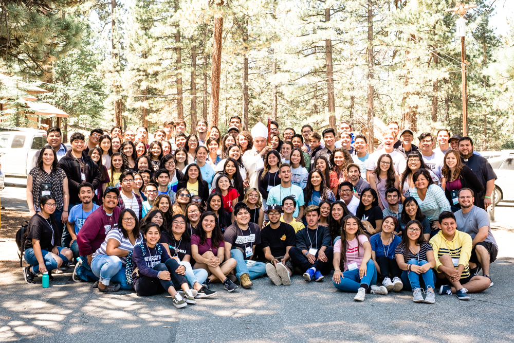 Large group of young Catholics gathered among pine trees