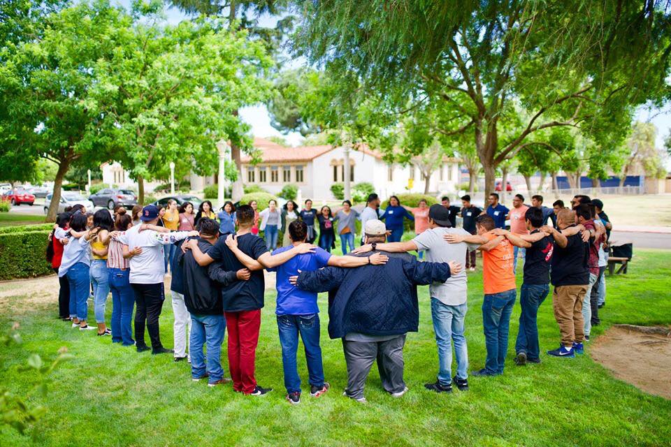 Group standing in a circle on the lawn with arms around each other